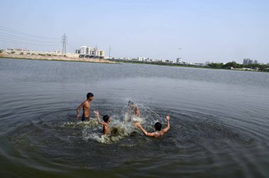 GURUGRAM, INDIA - 31 Mayıs 2024: Çocuklar sıcak bir yaz gününde, Hindistan 'ın Gurugram kentinde 31 Mayıs 2024' te, sektör-99 yakınlarındaki Dwarka Otoyolu 'nda sürmekte olan sıcak hava dalgasının ortasında, bir su birikintisinde banyo yaparken birbirlerine su sıçratırlar.. 
