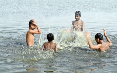 GURUGRAM, INDIA - 31 Mayıs 2024: Çocuklar sıcak bir yaz gününde, Hindistan 'ın Gurugram kentinde 31 Mayıs 2024' te, sektör-99 yakınlarındaki Dwarka Otoyolu 'nda sürmekte olan sıcak hava dalgasının ortasında, bir su birikintisinde banyo yaparken birbirlerine su sıçratırlar.. 