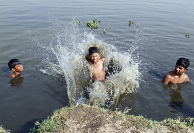 GURUGRAM, INDIA - 31 Mayıs 2024: Çocuklar sıcak bir yaz gününde, Hindistan 'ın Gurugram kentinde 31 Mayıs 2024' te, sektör-99 yakınlarındaki Dwarka Otoyolu 'nda sürmekte olan sıcak hava dalgasının ortasında, bir su birikintisinde banyo yaparken birbirlerine su sıçratırlar.. 