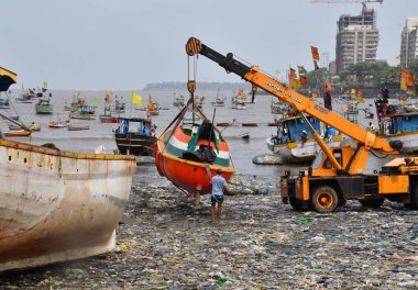 MUMBAI, INDIA - 27 Mayıs 2024 'te Hindistan' ın Mumbai kentindeki Badhwar Park 'ta, bir vinç kullanılarak deniz kıyısından çıkarılan bir tekne..