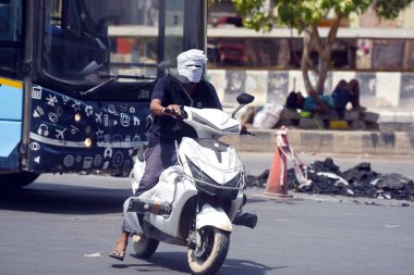 19 Mayıs 2024 'te Hindistan' ın Gurugram kentinde, Rajiv Chowk yakınlarında bir yaz öğleden sonra yol boyunca yol alırken, insanlar sıcaktan korunmak için yüzlerini kıyafetle örtüyorlar..