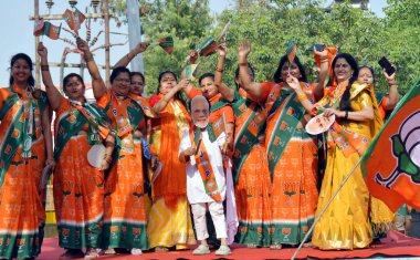 GHAZIABAD, INDIA - 6 Nisan 2024 'te Gaziabad Ambedkar Yolu' ndaki BJP yol gösterisinde sanatçılar ve destekçiler, Hindistan 'ın Gaziabad kentinde dans eden ve şarkı söyleyen kadın işçiler. Parti sembolü 'lotus' u elinde tutan Başbakan Modi,