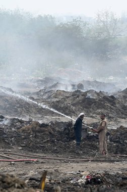 NOIDA, INDIA - 27 Mart 2024: İtfaiyeciler Sektör 32 'deki çöplük bahçesinde yangın söndürmeye çalışıyorlar. Pazartesi günü saat 18.00 sularında başlayan yangın, 32. Sektör 'de yaklaşık 1,5 km genişliğinde ve 2 km uzunluğunda bir alanı sardı.