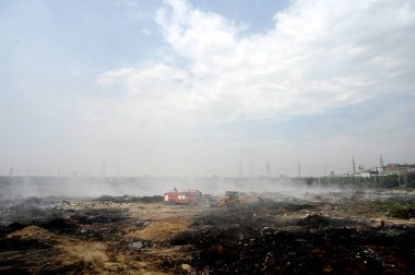 NOIDA, INDIA - 27 Mart 2024: İtfaiyeciler Sektör 32 'deki çöplük bahçesinde yangın söndürmeye çalışıyorlar. Pazartesi günü saat 18.00 sularında başlayan yangın, 32. Sektör 'de yaklaşık 1,5 km genişliğinde ve 2 km uzunluğunda bir alanı sardı.
