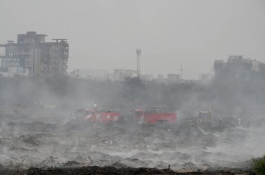 NOIDA, INDIA - 27 Mart 2024: İtfaiyeciler Sektör 32 'deki çöplük bahçesinde yangın söndürmeye çalışıyorlar. Pazartesi günü saat 18.00 sularında başlayan yangın, 32. Sektör 'de yaklaşık 1,5 km genişliğinde ve 2 km uzunluğunda bir alanı sardı.