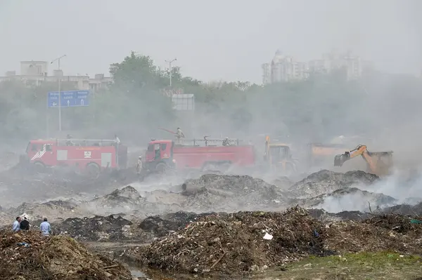 NOIDA, INDIA - 27 Mart 2024: İtfaiyeciler Sektör 32 'deki çöplük bahçesinde yangın söndürmeye çalışıyorlar. Pazartesi günü saat 18.00 sularında başlayan yangın, 32. Sektör 'de yaklaşık 1,5 km genişliğinde ve 2 km uzunluğunda bir alanı sardı.