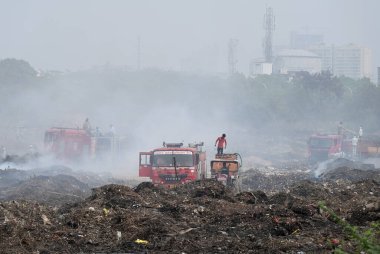 NOIDA, INDIA - 27 Mart 2024: İtfaiyeciler Sektör 32 'deki çöplük bahçesinde yangın söndürmeye çalışıyorlar. Pazartesi günü saat 18.00 sularında başlayan yangın, 32. Sektör 'de yaklaşık 1,5 km genişliğinde ve 2 km uzunluğunda bir alanı sardı.