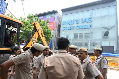 NEW DELHI, INDIA - JULY 29, 2024: Police personnel guard as a bulldozer demolishes parts of the IAS coaching institute in Old Rajinder Nagarafter three civil services aspirants died at a coaching centre due to drowning. clipart