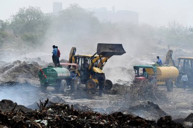 NOIDA, INDIA - 27 Mart 2024: İtfaiyeciler Sektör 32 'deki çöplük bahçesinde yangın söndürmeye çalışıyorlar. Pazartesi günü saat 18.00 sularında başlayan yangın, 32. Sektör 'de yaklaşık 1,5 km genişliğinde ve 2 km uzunluğunda bir alanı sardı.