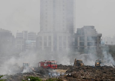 NOIDA, INDIA - 27 Mart 2024: İtfaiyeciler Sektör 32 'deki çöplük bahçesinde yangın söndürmeye çalışıyorlar. Pazartesi günü saat 18.00 sularında başlayan yangın, 32. Sektör 'de yaklaşık 1,5 km genişliğinde ve 2 km uzunluğunda bir alanı sardı.