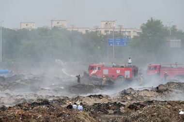 NOIDA, INDIA - 27 Mart 2024: İtfaiyeciler Sektör 32 'deki çöplük bahçesinde yangın söndürmeye çalışıyorlar. Pazartesi günü saat 18.00 sularında başlayan yangın, 32. Sektör 'de yaklaşık 1,5 km genişliğinde ve 2 km uzunluğunda bir alanı sardı.