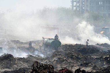 NOIDA, INDIA - 27 Mart 2024: İtfaiyeciler Sektör 32 'deki çöplük bahçesinde yangın söndürmeye çalışıyorlar. Pazartesi günü saat 18.00 sularında başlayan yangın, 32. Sektör 'de yaklaşık 1,5 km genişliğinde ve 2 km uzunluğunda bir alanı sardı.