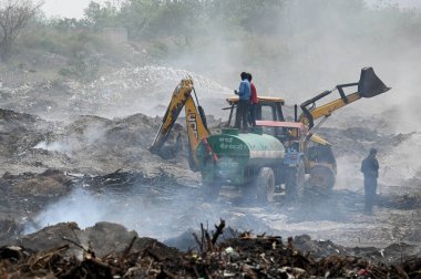 NOIDA, INDIA - 27 Mart 2024: İtfaiyeciler Sektör 32 'deki çöplük bahçesinde yangın söndürmeye çalışıyorlar. Pazartesi günü saat 18.00 sularında başlayan yangın, 32. Sektör 'de yaklaşık 1,5 km genişliğinde ve 2 km uzunluğunda bir alanı sardı.