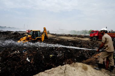 NOIDA, INDIA - 27 Mart 2024: İtfaiyeciler Sektör 32 'deki çöplük bahçesinde yangın söndürmeye çalışıyorlar. Pazartesi günü saat 18.00 sularında başlayan yangın, 32. Sektör 'de yaklaşık 1,5 km genişliğinde ve 2 km uzunluğunda bir alanı sardı.