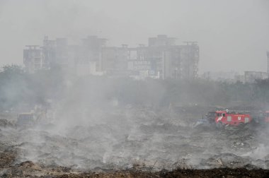 NOIDA, INDIA - 27 Mart 2024: İtfaiyeciler Sektör 32 'deki çöplük bahçesinde yangın söndürmeye çalışıyorlar. Pazartesi günü saat 18.00 sularında başlayan yangın, 32. Sektör 'de yaklaşık 1,5 km genişliğinde ve 2 km uzunluğunda bir alanı sardı.