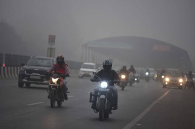 GURUGRAM, INDIA JANUARY 24: Gurugram-Sohna 'da seyahat ederken sıcak kıyafetler giydikleri görülen banliyö sakinleri, 24 Ocak 2024' te Hindistan 'ın Gurugram kentinde, Hava Üssü yakınlarındaki soğuk ve sisli kış sabahında ekspres yolda yükseldiler.