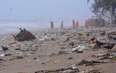 MUMBAI, INDIA - 5 Temmuz 2023 tarihinde Hindistan 'ın Mumbai kentinde Juhu sahilinde muson mevsiminde yıkanan plastik atıkları ve çöpleri temizleyen sivil işçiler. Şehrin sahil şeridi, insanlar çöplerini atarken ciddi bir çöp krizine tanık oluyor.