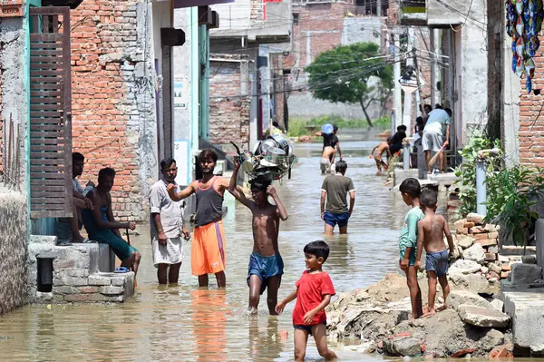 GREATER NOIDA, INDIA - 24 Temmuz 2023 'te Hindistan' ın başkenti Büyük Noida 'da bulunan Purana Haibatpur köyünde, daha güvenli bir yere taşınırken, Hindon nehrinin etrafındaki alçak bölgelerden gelen insanlar taşan sel sularından yürüyerek geçtiler. Fotoğraf: Su