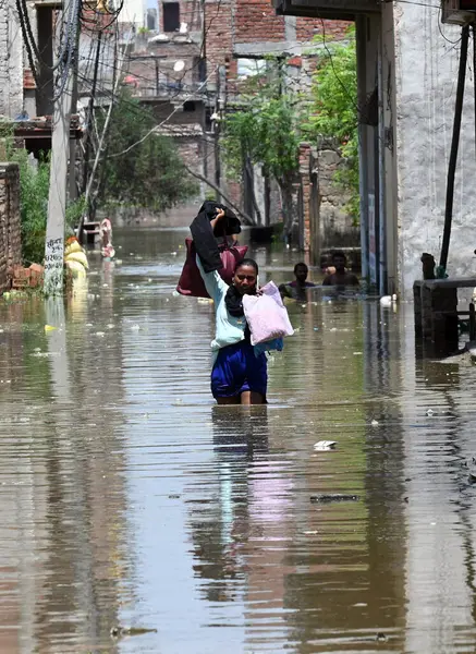 GREATER NOIDA, INDIA - 24 Temmuz 2023 'te Hindistan' ın başkenti Büyük Noida 'da bulunan Purana Haibatpur köyünde, daha güvenli bir yere taşınırken, Hindon nehrinin etrafındaki alçak bölgelerden gelen insanlar taşan sel sularından yürüyerek geçtiler. Fotoğraf: Su