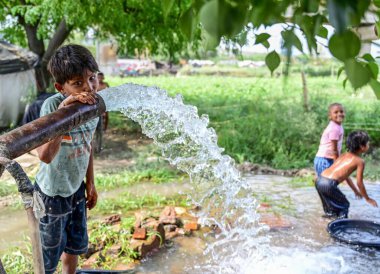 NEW DELHI INDIA - 3 Haziran 2024 Yeni Delhi Hindistan 'da 3 Haziran 2024 tarihinde Yamuna sel yatakları boyunca sıcak bir yaz günü öğleden sonra sıcak hava dalgasından biraz rahatlamak için su pompasının altında oynayan çocuklar. (Fotoğraf: Vipin Kumar / Hindustan Times 