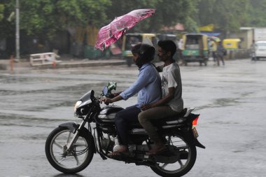 GURUGRAM INDIA 25 HAZİRAN 2023 Bir sütun binicisi şemsiye tutarken scootercı Kahraman Honda Chowk 'ta 25 Haziran 2023' de Gurugram Hindistan 'da yağmurda yol alırken şimşekler eşliğinde başkent Delhi' nin çeşitli bölgelerine ve