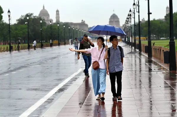 NEW DELHI INDIA 25 HAZİRAN 2023 Ziyaretçiler ve sabah yürüyüşçüleri 25 Haziran 2023 Hindistan Kapısı yakınlarındaki hafif yağmurun keyfini çıkarıyorlar Yeni Delhi Hindistan 'da sağanak yağış ile birlikte ulusal başkent Delhi' nin bazı bölgelerini ve bitişik sanayi bölgelerini yıldırımlar vurdu.