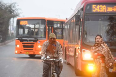 NEW DELHI INDIA JANUARY 7: 2024 Soğuk bir kış sabahı MCD Ofisi yakınlarındaki Güney Batı Delhi Kapashera otobüs durağında otobüs bekleyen Kuzey Hindistan 'da gittikçe artan soğuk hava dalgası civa dalgıçları ile Delhi NCR' ye meydan okuyor. 