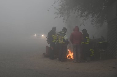 NEW DELHI INDIA 14 HAZİRAN 2024 soğuk ve yoğun bir kış sabahı Samalkha yakınlarındaki Güney Batı Delhi 'de bir şenlik ateşinin yanında insanlar ısınıyor sisli bir sabah Delhi NCR ile yoğun soğuk hava dalgası civaları Kuzey Hindistan' da daha da derinleşiyor.