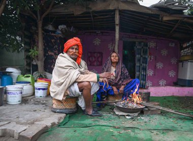 GURUGRAM INDIA JANUARY 15 2024 An old man and woman sit next to a bonfire on a cold winter morning at Kadipur road near Government Senior Secondary School Foggy morning challenges Delhi NCR with intensifying cold wave mercury dips further across Nort clipart