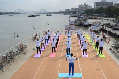 KOLKATA INDIA JUNE 21 2023 Port Trust officials participate in an event on the occasion of 9th International Day of Yoga on board P S Bhopal at Outram Jetty on banks of river Hooghly against backdrop of iconic Howrah Bridge on June 21 2023 in Kolkata clipart