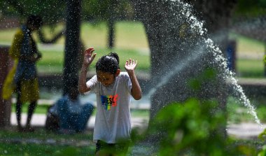 NEW DELHI INDIA 18 Nisan 2023 Bir kız Hindistan 'da 18 Nisan 2023' te Delhi NCR 'de sıcaklık yükselirken Hindistan kapısında sıcak bir günde su fıskiyelerinden su püskürten bir kızın keyfini çıkarıyor Yeni Delhi' de maksimum sıcaklık 40 derece.