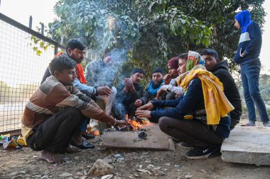 GURUGRAM, INDIA - 14 Aralık 2024 'te Hindistan' ın Gurugram kentinde, Leisure Valley Park yakınlarındaki soğuk bir kış sabahı kendilerini korumak için şenlik ateşinin etrafında oturan insanlar. 