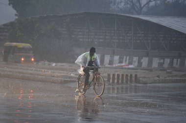 GURUGRAM, INDIA - 27 Aralık 2024: İnsanlar 27 Aralık 2024 'te Hindistan' ın Gurugram kentinde, bölge mahkemesi yakınlarındaki Rajiv Chowk 'ta kış sabahı yağmur yağarken işyerlerine gidiyorlar. Delhi ve yakındaki bölgelere Cuma günü orta şiddette yağmur yağdı. 