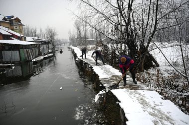 SRINAGAR INDIA JANUARY 6. 2025 İşçiler, 6 Ocak 2025 'te Srinagar Hindistan' da kar yağışı sonrasında Dal Gölü 'nün içindeki tahta ayak köprüsünden karları kaldırdı.