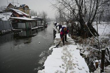 SRINAGAR INDIA JANUARY 6. 2025 İşçiler, 6 Ocak 2025 'te Srinagar Hindistan' da kar yağışı sonrasında Dal Gölü 'nün içindeki tahta ayak köprüsünden karları kaldırdı.