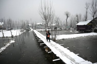 6 Ocak 2025 'te Srinagar Hindistan' da kar yağışı sonrası Dal Gölü 'nün iç kısımlarında karla kaplı tahta köprü üzerinde yürürken bir adam bir çocuk taşıyor. Fotoğraf: Waseem Andrabi Hindustan Times