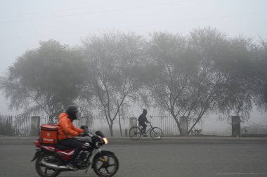 GURUGRAM INDIA JANUARY 4. 2025 İnsanlar sıcak kıyafetler giyip 4 Ocak 2025 'te Gurugram Hindistan' da Ambience Alışveriş Merkezi yakınlarındaki 48 numaralı Ulusal Otoyol 'daki soğuk ve yoğun sis koşullarında çalışmaya gidiyorlar.
