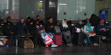 NEW DELHI INDIA JANUARY 4 2025 Passengers sit on a platform covering themselves with woolen cloths at New Delhi Railway Station several train services are impacted due to dense fog on January 4 2025 in New Delhi India A dense blanket of fog once agai clipart