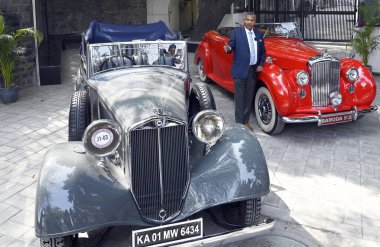 NEW DELHI INDIA FEBRUARY 11 2025 21 Gun Salute Heritage and Cultural Trust Founder and Managing Trustee Madan Mohan poses for a picture with a Vintage Car during a press conference ahead of the 11 edition of 21 Gun Salute Concours Delegance Vintage C clipart