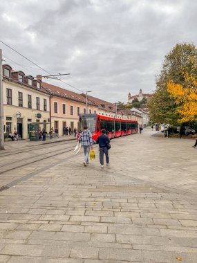 A red electric tram traveling through the streets of Bratislava Old Town, Slovakia showing Bratislava Castle in the Background clipart