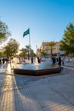 Arka planda Suudi bayrağı olan bir Riyad Çeşmesi Günbatımı Manzarası. Çeşme, Suudi Arabistan 'ın Riyad ilinin Ad Dirah ilçesinde Al-Safat Meydanı yakınlarında yer almaktadır. Günbatımı Suudi bayrağı için güzel bir zemin sağlar..
