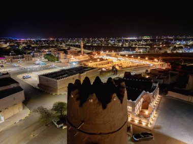 Aerial night drone view of Shaqra showcasing illuminated cityscapes, historic Najdi architecture, and prominent cultural landmarks.