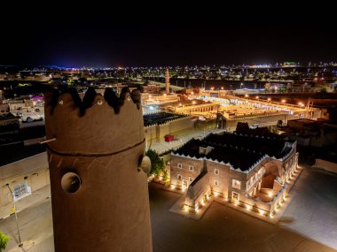 Shaqra 'nın hava gece drone görüntüsü aydınlatılmış şehir manzaraları, tarihi Najdi mimarisi ve önemli kültürel simgeler.