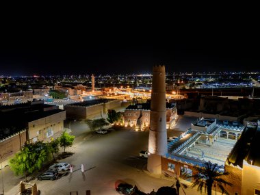 Aerial night drone view of Shaqra showcasing illuminated cityscapes, historic Najdi architecture, and prominent cultural landmarks.
