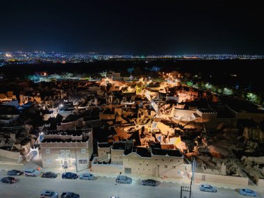 Aerial night drone view of Shaqra showcasing illuminated cityscapes, historic Najdi architecture, and prominent cultural landmarks.