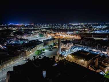 Shaqra 'nın hava gece drone görüntüsü aydınlatılmış şehir manzaraları, tarihi Najdi mimarisi ve önemli kültürel simgeler.