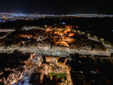 Aerial night drone view of Shaqra showcasing illuminated cityscapes, historic Najdi architecture, and prominent cultural landmarks.