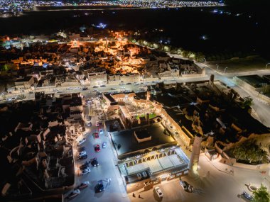 Aerial night drone view of Shaqra showcasing illuminated cityscapes, historic Najdi architecture, and prominent cultural landmarks.
