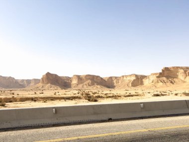 Riyad yakınlarındaki çöl manzarası, Suudi Arabistan. Yuvarlanan kum tepeleri, kayalık kayalıklar ve kuru arazi Arap Yarımadası 'nın kurak ortamının ham güzelliğini yakalıyor..