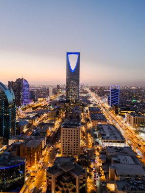 Günbatımında Suudi Arabistan 'daki Riyad şehrinin aydınlanmış insansız hava aracı fotoğrafı. Sergide kent simgeleri, modern ufuk çizgisi, önemli kuleler ve şehir tasarımı sergileniyor..